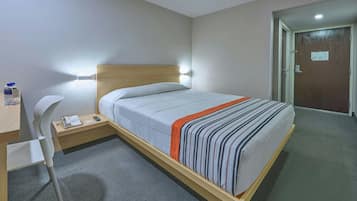 Habitación de hotel con cama, mesita de noche, silla y escritorio, además de teléfono y botella de agua.