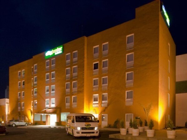Et hotel med gul facade, mange vinduer og en hvid varevogn foran.