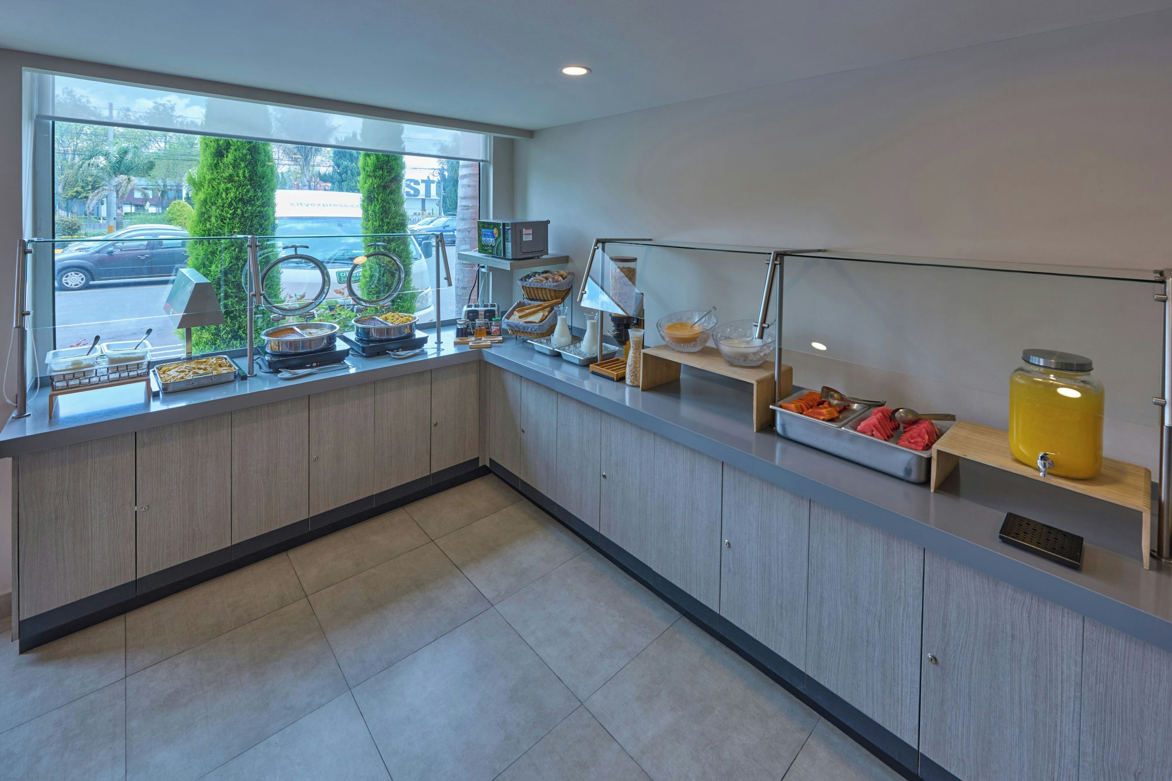 A modern kitchen with a breakfast bar, various food items, and a view of the street through a large window.