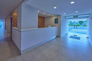 Zona de recepción con mostrador, tablón informativo en la pared y puerta que da al exterior.