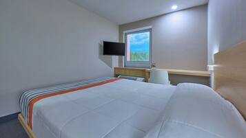 Habitación de hotel con cama, televisor de pantalla plana en la pared, ventana con vista a zonas verdes y mesita de noche con lámpara.