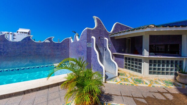 A swimming pool with a tiled deck, a palm plant, and a building with a tiled facade. - Hotel Isla de Sacrificio (Veracruz)
