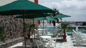 A rooftop terrace with white plastic chairs and tables, green umbrellas, and potted plants. - Hotel Isla de Sacrificio (Veracruz)
