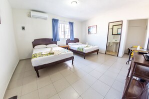 Habitación de hotel con dos camas individuales, un escritorio con silla, baño con lavamanos y espejo, y ventana con cortinas.