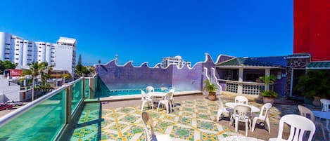 A rooftop terrace with a pool, outdoor seating, and a view of the cityscape.