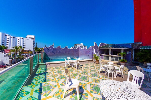 Una terraza en la azotea con piscina, asientos exteriores y vistas a la ciudad.