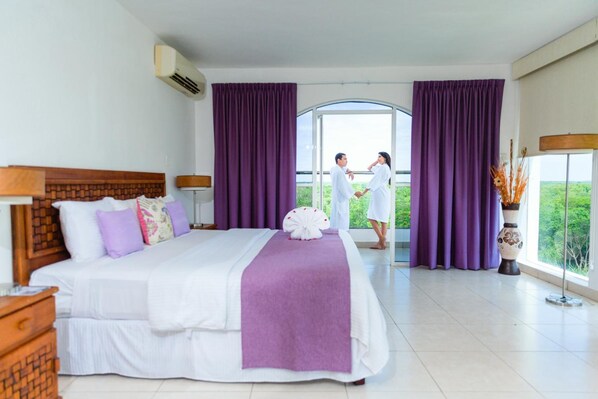 A hotel room with a large bed, purple curtains, a view of greenery, and a vase with dried plants. - Uxmal Resort Maya (Muna)