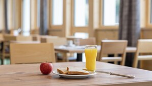 Una mesa con una tostada, un vaso de jugo de naranja y una manzana.