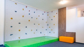 A climbing wall with various colored holds, a green padded mat, and a wooden panel wall.