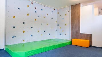 A climbing wall with various colored holds, a green padded mat, and a wooden panel wall.