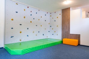 A climbing wall with various colored holds, a green padded mat, and a wooden panel wall. - Hotel Tia Smart Natur (Kaunertal)