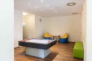 Una habitación con mesa de fútbol de mesa, dos sillones de peluche, una mesita y un banco verde.