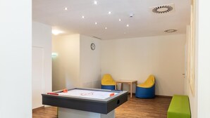 Una habitación con mesa de fútbol de mesa, dos sillones de peluche, una mesita y un banco verde.
