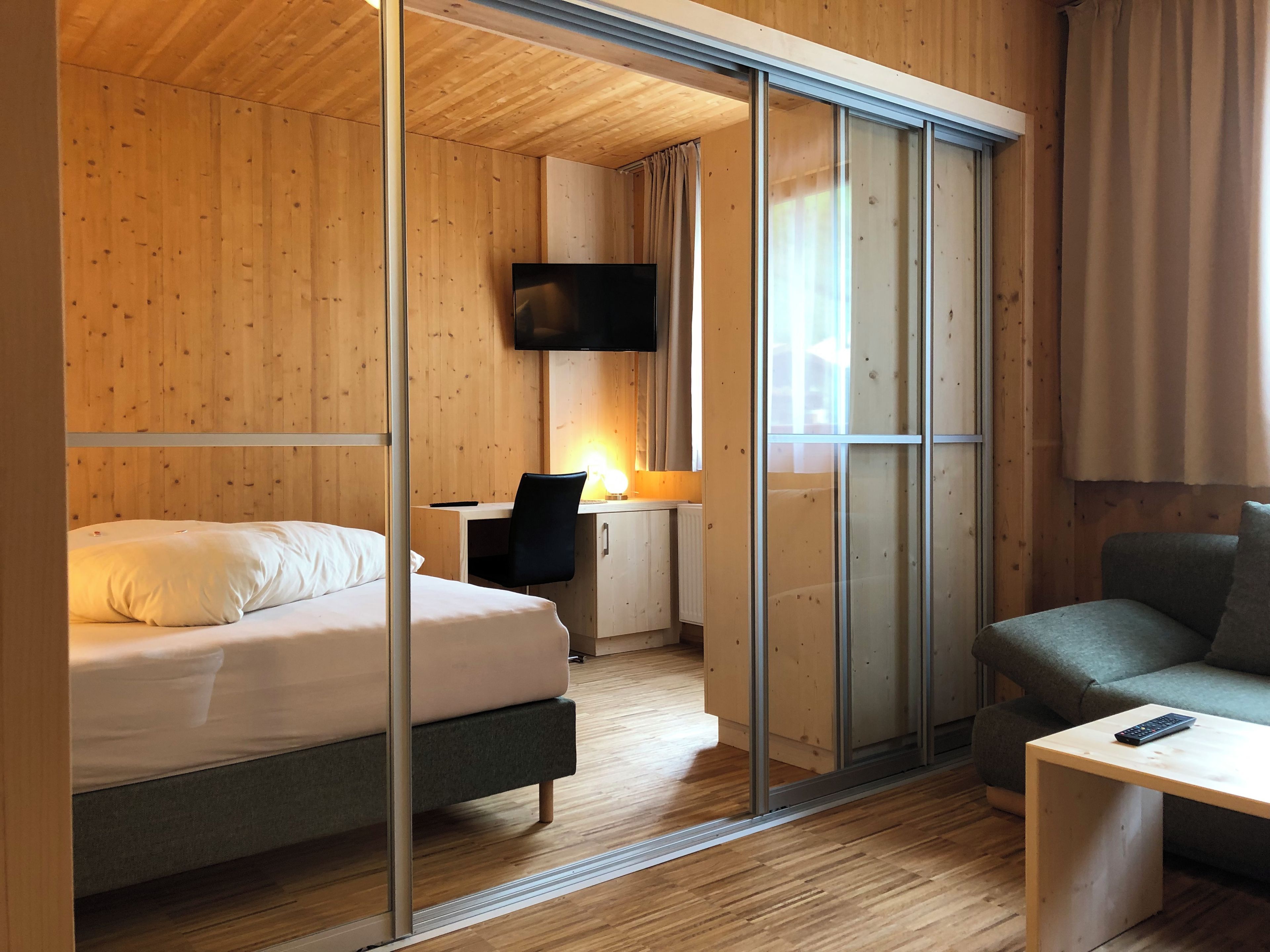 Ein modernes Hotelzimmer mit Holzvertäfelung, einem Bett, einem Schreibtisch mit Stuhl, einem Fernseher und einem Sofa.