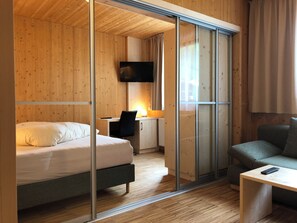 A modern hotel room with a wooden interior, a bed, a desk with a chair, a television, and a sofa. - Hotel Tia Smart Natur (Kaunertal)