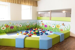 Un área de juegos infantiles con bloques de construcción de colores y un mural con flores e insectos en la pared.