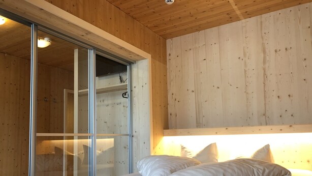Un dormitorio moderno con techo de madera, una cama grande con ropa blanca y una puerta corrediza de vidrio que da a un baño.