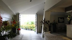 A spacious hallway with a patterned sofa, potted plants, and a view of greenery outside.