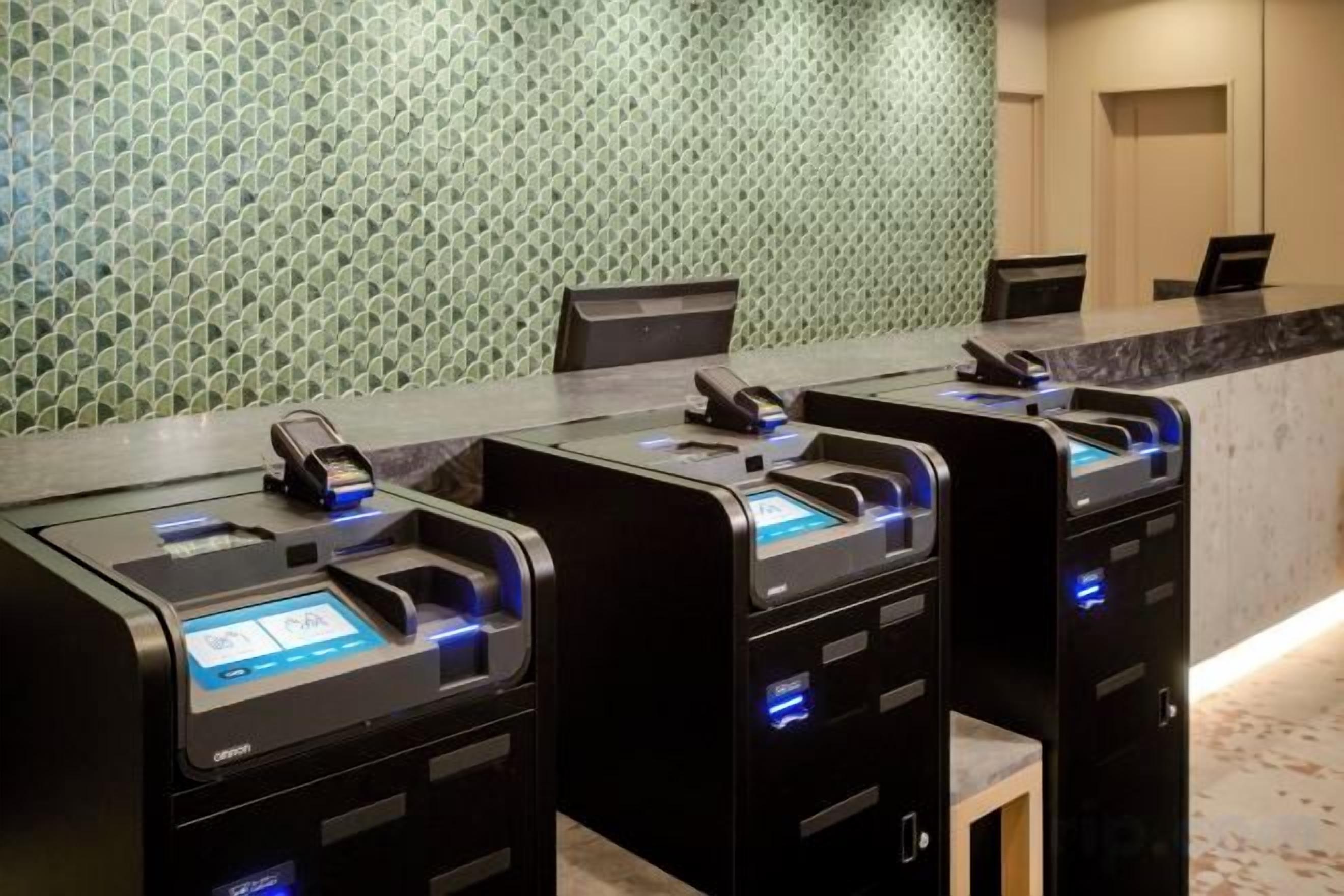Zona de recepción con mostrador, teléfono y tres quioscos de autoservicio.