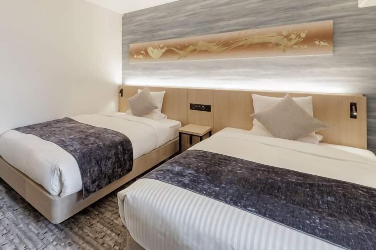 Habitación de hotel con dos camas, un cabecero moderno, una obra de arte colgada en la pared y una mesita de noche pequeña.