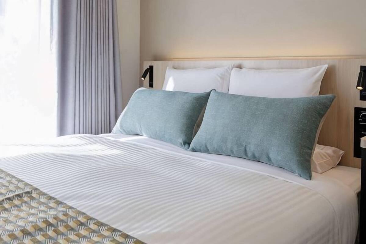 Una cama bien hecha con una colcha estampada, dos almohadas y un cabecero con luces empotradas.