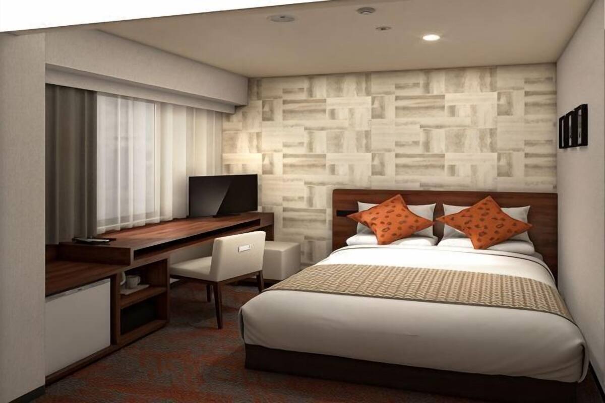 Habitación de hotel con cama, escritorio con televisor, una silla y un diseño decorativo en la pared.