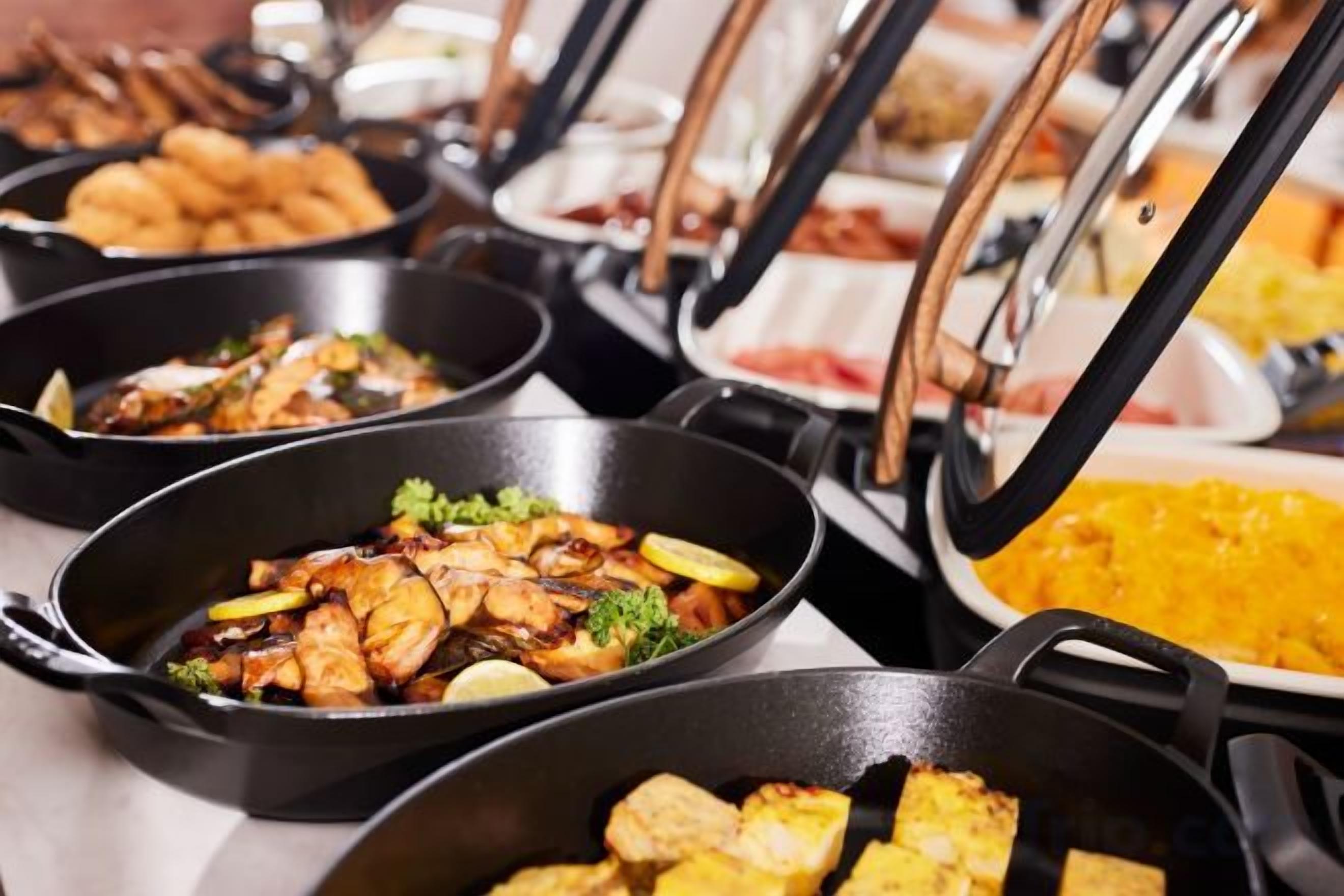 Un buffet con diversi piatti presentati in pentole nere, tra cui sembra esserci pollo fritto e un piatto di riso giallo.