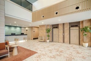 Eine Hotelhalle mit Empfangstresen, einer Sitzecke und einer hohen Decke mit Holzlamellen.