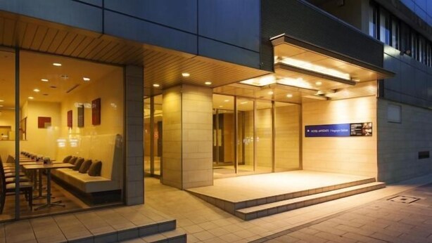 Entrada de hotel com balcão de recepção, área de estar e placa com o nome do hotel.