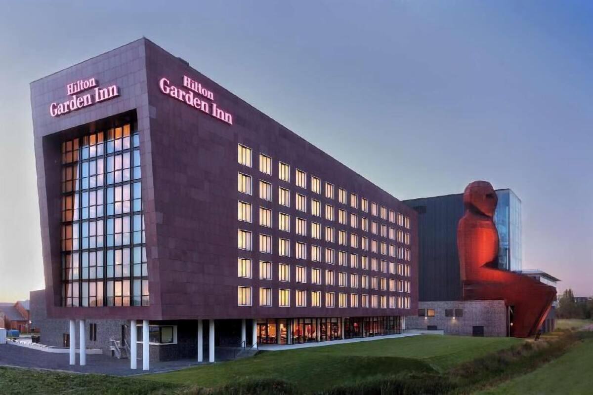 Um Hilton Garden Inn com design moderno, janelas amplas e uma escultura marcante.
