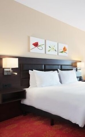 A hotel room with a bed, a nightstand, a lamp, and wall art. - Hilton Garden Inn Leiden (Oegstgeest)