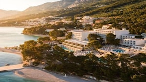 Ein Küstenhotel mit mehreren Gebäuden, einem Strand und einer Bergkulisse im Hintergrund.