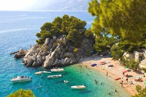 A coastal beach with boats, people, and a building with a stone facade. - Bluesun Mala Berulia (Brela)