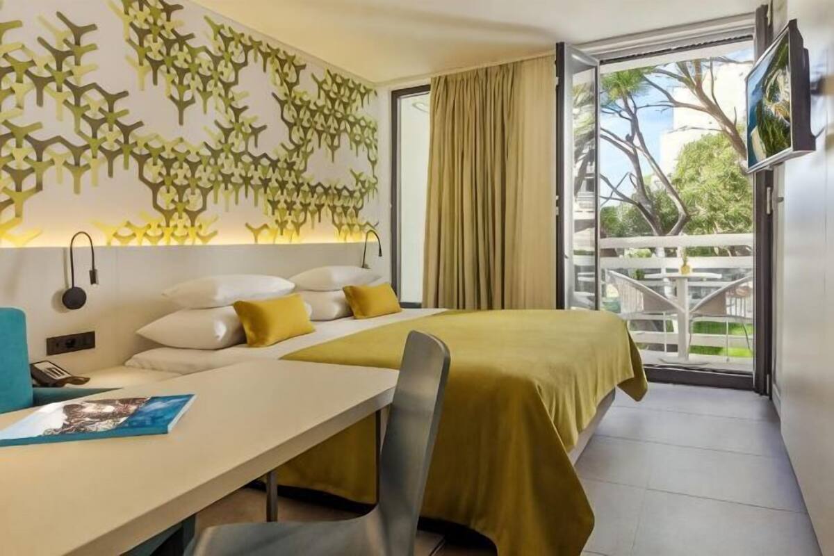 A hotel room with a bed, a desk, a chair, a TV, and a balcony with a view.