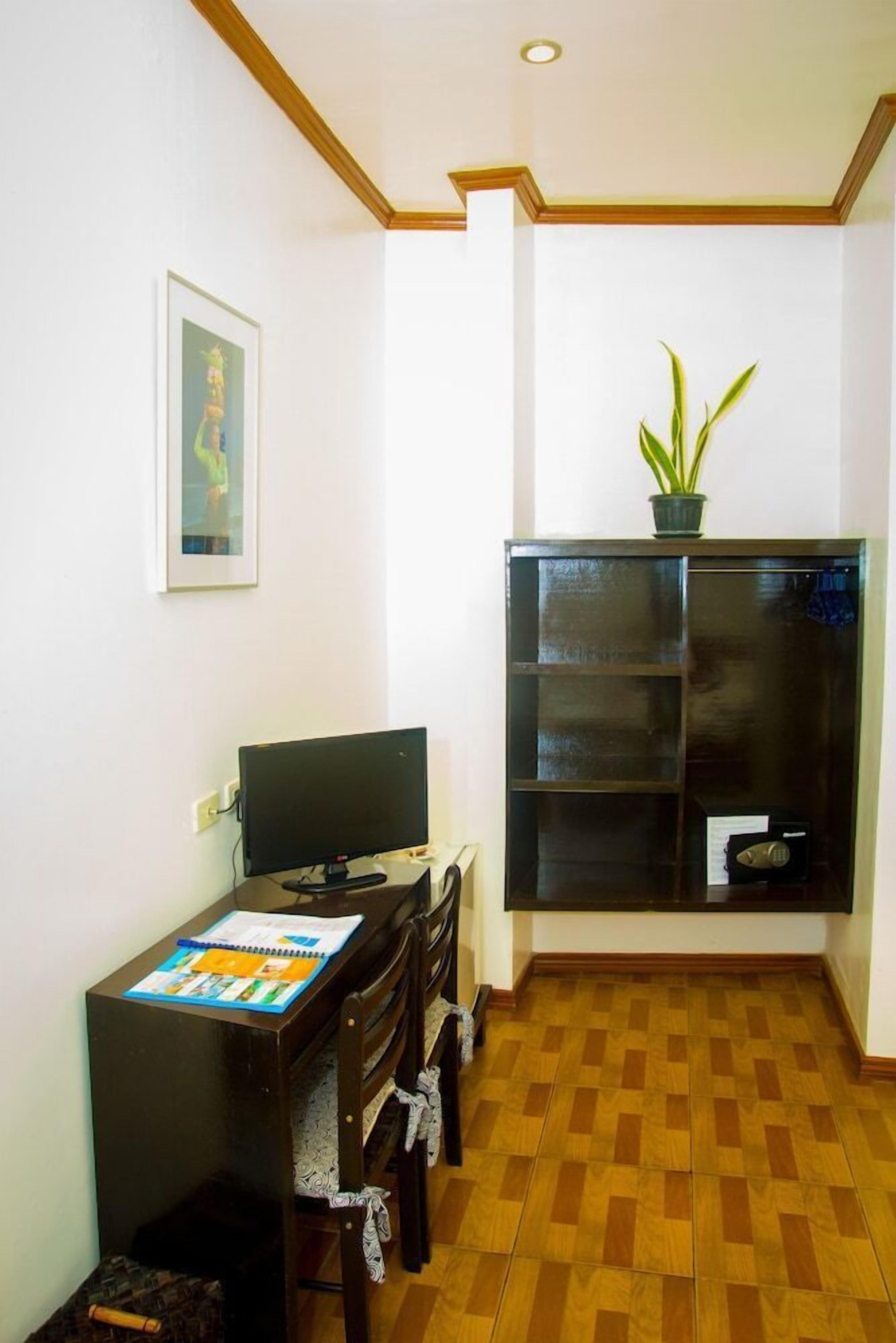 Una habitación con escritorio, una silla, computadora, estantería y una planta en maceta.