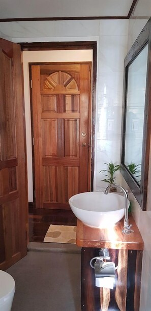 Un baño con puerta de madera, un lavabo blanco y un espejo.