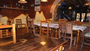 Interior de restaurante con mesas y sillas de madera, copas de vino y lámparas colgantes.