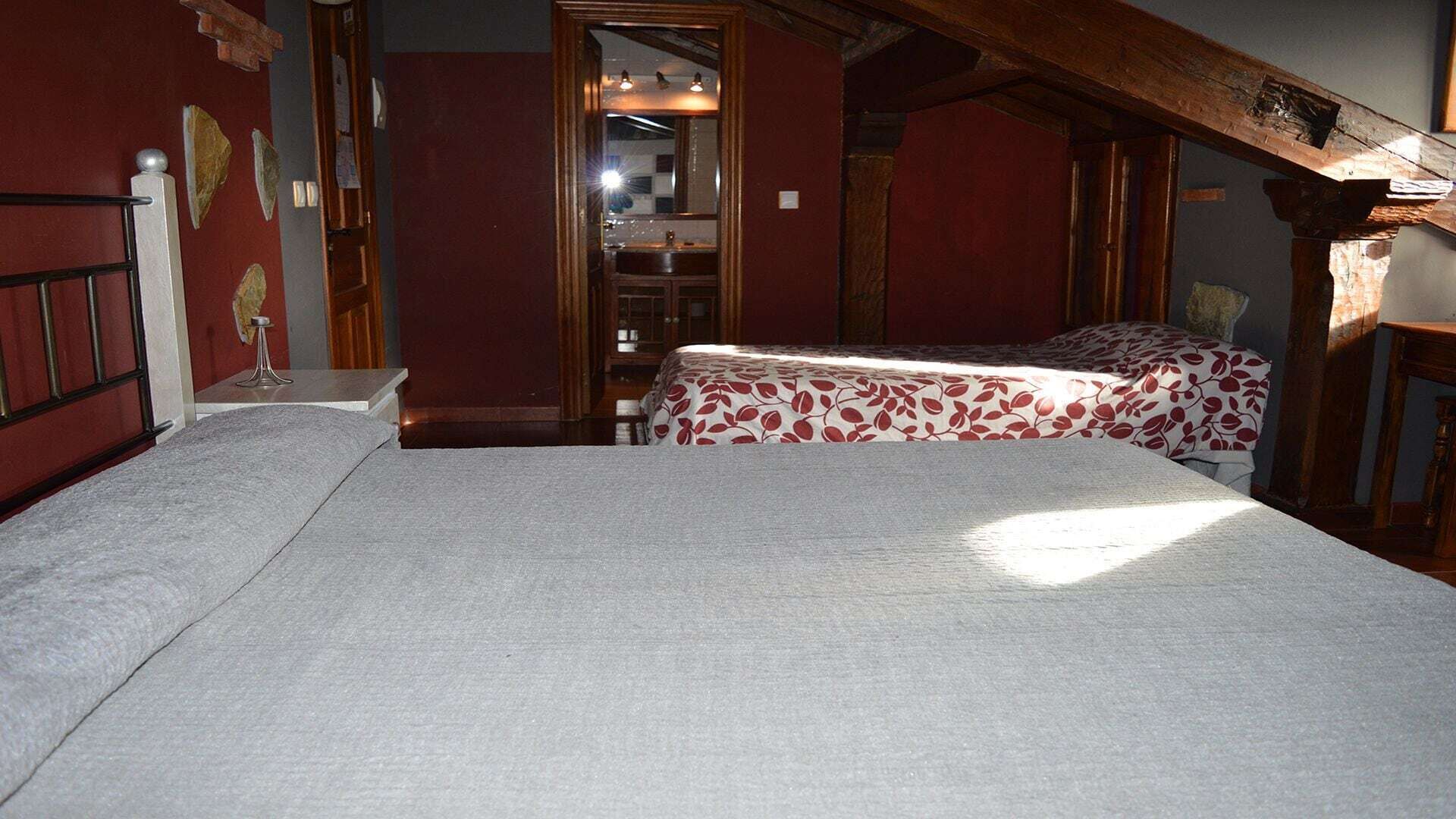 A room with two beds, a wooden ceiling, and a mirror.