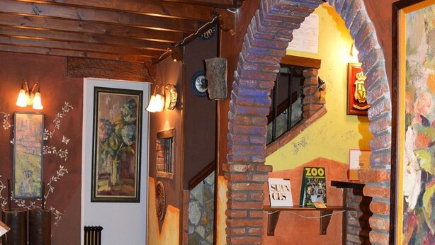 Un vestíbulo con piso a cuadros, vigas de madera, un arco de ladrillo y una escalera que lleva a un nivel superior.