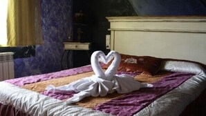 Una cama con una manta blanca, un plaid morado, una almohada marrón y un arreglo de toallas con forma de corazón.