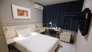 A hotel room with a bed, a desk, a chair, a desk lamp, a small cabinet, an air conditioning unit, and a curtain. - Jinjiang Inn (Shanghai)