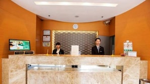 A reception desk with two staff members, a clock, and a television screen. - Jinjiang Inn (Shanghai)