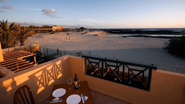 Une terrasse avec une table dressée pour deux personnes, offrant une vue sur la plage et la mer.