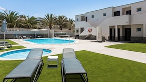 Une piscine avec deux chaises longues, une bouée de sauvetage et un bâtiment doté de nombreuses fenêtres et portes.