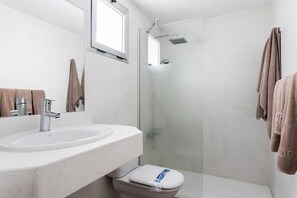 A modern bathroom with a white sink, a toilet, and a glass-enclosed shower. - Cotillo Sunset (La Oliva)