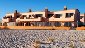 Un hôtel situé en bord de mer, doté de nombreux balcons, de grandes fenêtres et d’une plage de sable en contrebas.