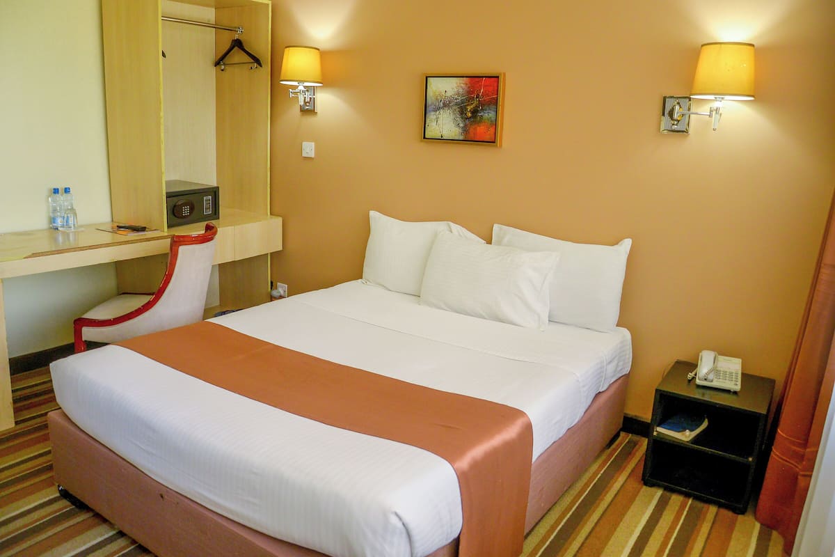 A hotel room with a bed, a desk, a chair, a nightstand, and a painting on the wall.