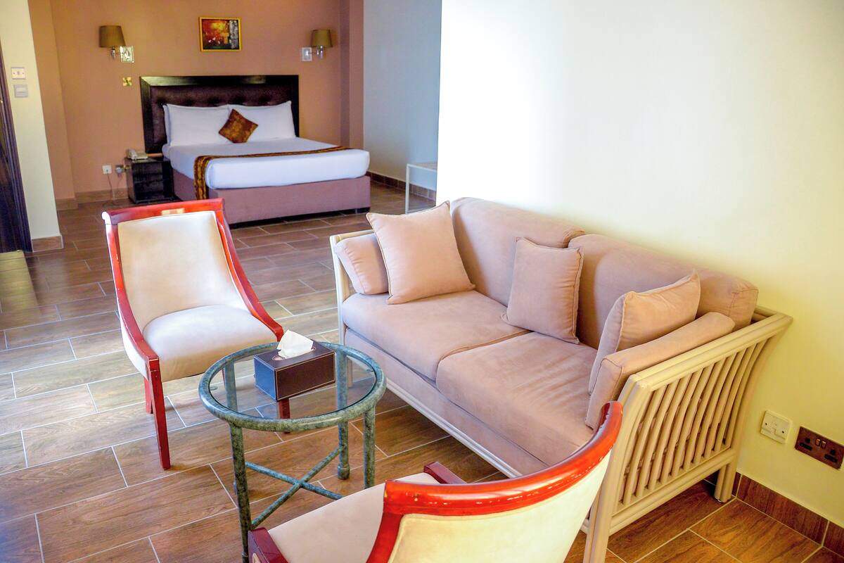 A hotel room with a bed, a sofa, two armchairs, a glass coffee table, and a radiator.
