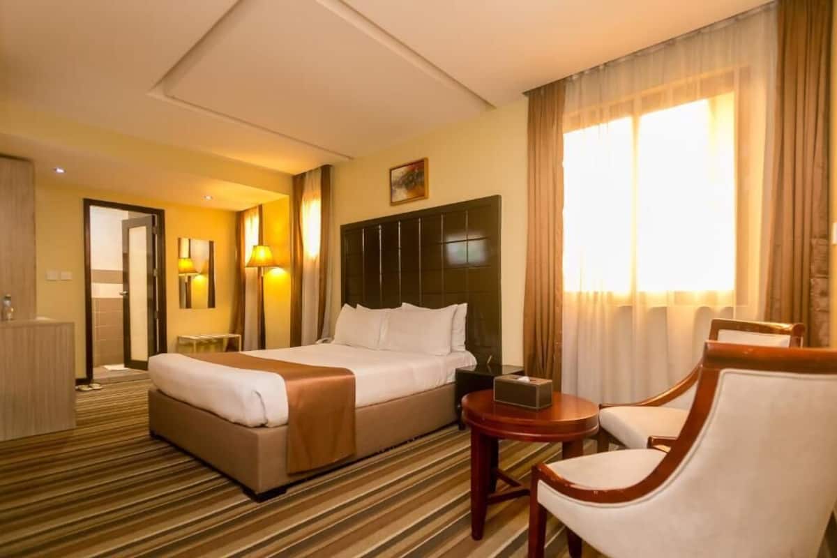 A hotel room with a large bed, a bedside table, a chair, and a small table.