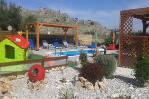 Un área de piscina con sillones de descanso, una pérgola de madera y una casita de juegos.